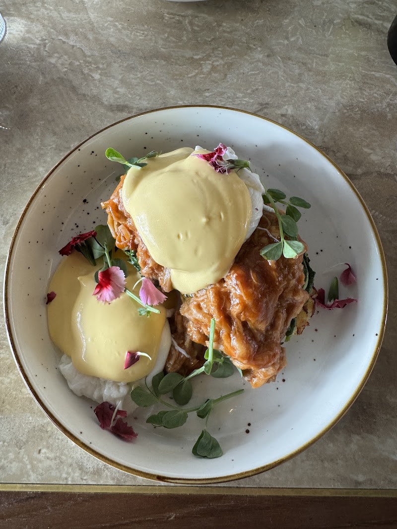 poached eggs draped in hollandaise sauce over a crispy filling, garnished with microgreens and edible flowers â Moonchild Bistro, Prahran