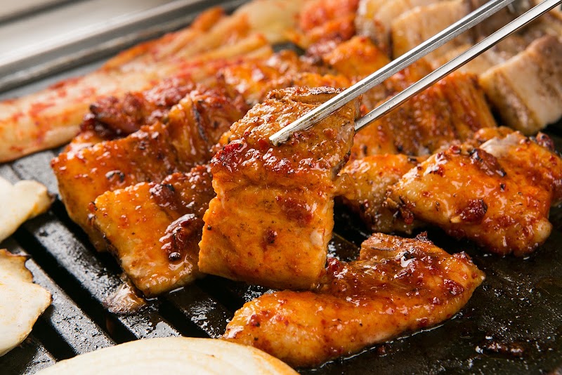marinated meat sizzling on a tabletop grill, tongs lifting a glazed piece â The Zungle, Parramatta