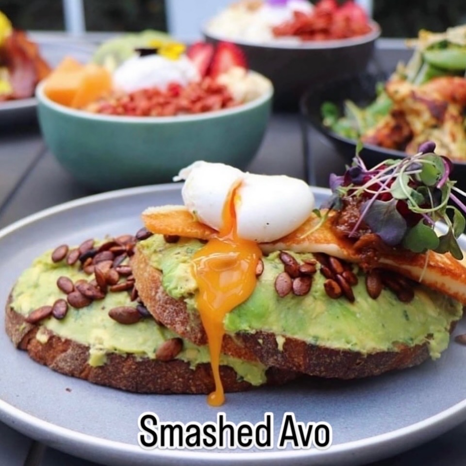 smashed avocado on sourdough with pepitas, halloumi and a running poached egg; venue's own 'Smashed Avo' caption sits on the plate rim â Fourth Chapter, Prahran